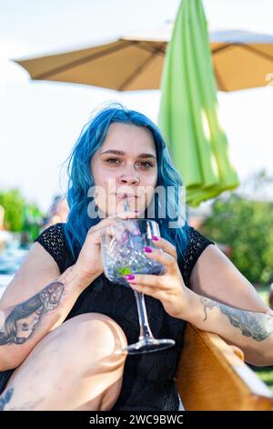 Ein junges erwachsenes Mädchen, das ein Glas hält und einen kalten Gin Tonic Cocktail durch einen Strohhalm trinkt Stockfoto