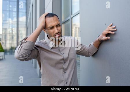 Besorgter junger Mann in legeren Business-Kleidern, der sich an eine Stadtmauer lehnt und in einer Stadt gestresst oder desorientiert aussieht. Stockfoto
