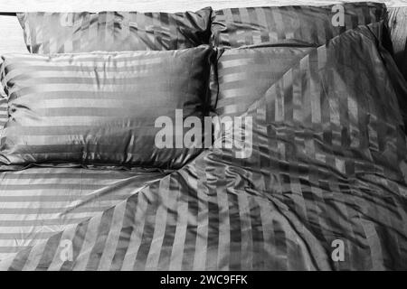 Leeres Bett mit gestreifter Satin-Bettwäsche in Nahaufnahme, Schwarzweißfoto Stockfoto