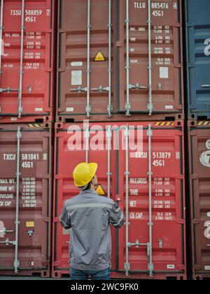 Porträt eines Ingenieur-Mannes, der einen Sicherheitshelm trägt, während er vor dem Frachtschiff des Containers steht. Stockfoto