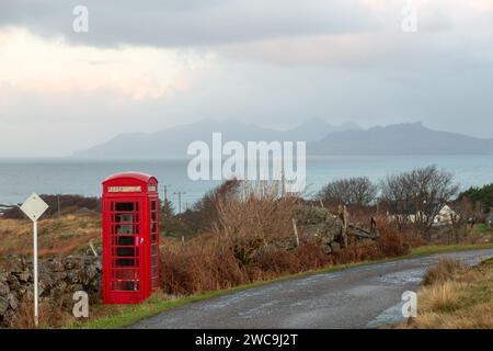 Eine rote britische Telefonzelle auf einer abgelegenen einspurigen Straße auf der Ardnamurchan-Halbinsel mit den Inseln Rum und Eigg im Hintergrund Stockfoto