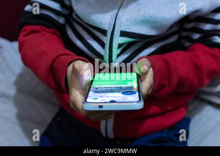 Das Kind klopft mit dem Finger auf den Bildschirm des Mobiltelefons, während es nachts zu Hause Online-Spiele aus einem anderen Blickwinkel spielt Stockfoto