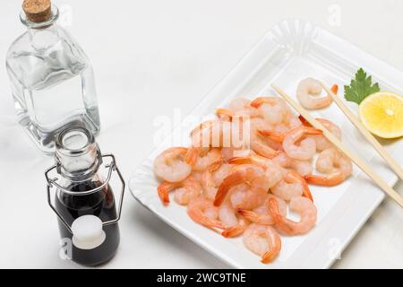 Garnelen mit Zitrone auf weißer Platte. Sojasauce und Wasser in Glasflaschen. Weißer Hintergrund. Draufsicht Stockfoto
