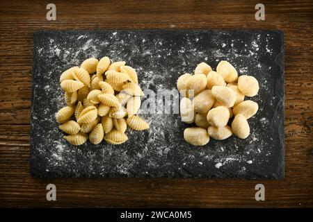 Blick von oben auf rohe, ungekochte, hausgemachte italienische Gnocchetti sardi und Gnocchi-Pasta auf schwarzem Brett mit Mehl Stockfoto