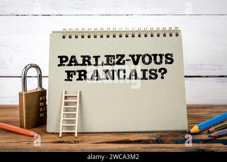 Sprechen Sie Französisch? In französischer Sprache verfasst. Grüner Notizblock auf Holztisch mit Textur und weißem Hintergrund. Stockfoto