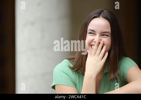 Vorderansicht Porträt einer glücklichen Frau, die lacht und den Mund mit der Hand auf der Straße versteckt Stockfoto