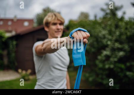 Mann mittleren Alters, der im Garten Kraftübungen mit Widerstandsband macht. Konzept der Trainingsroutine zu Hause. Stockfoto