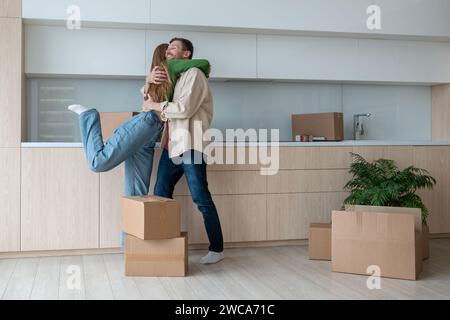 Glückliche, überglückte Frau und Mann umarmten sich in der Küche und zogen in eine neue Wohnung zwischen Pappkartons Stockfoto