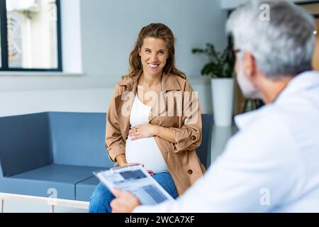Schließen Sie eine schwangere Frau, die mit einem Geburtshelfer im Krankenhaus spricht und ihren Bauch hält. Arzt und zukünftige Mutter sprechen über Geburt, geplanter Kaiserschnitt Stockfoto