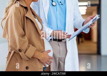 Schließen Sie eine schwangere Frau, die mit einem Geburtshelfer im Krankenhaus spricht und ihren Bauch hält. Arzt und zukünftige Mutter sprechen über Geburt, geplanter Kaiserschnitt Stockfoto
