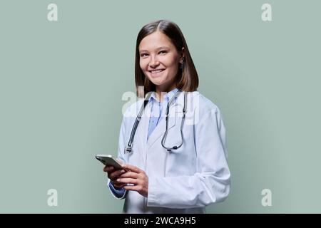 Junge Ärztin mit Smartphone, auf grünem Atelierhintergrund Stockfoto