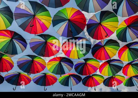 Das Bild fängt den Anblick zahlreicher farbenfroher Regenschirme ein, die in der Luft hängen. Die Regenschirme sind mehrfarbig, jeder mit einer einzigartigen Kombination von en Stockfoto