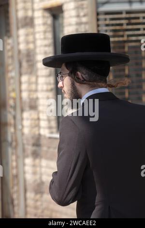 Ein orthodoxer jüdischer Mann in Brooklyn geht in den Wind, mit seinem Lockenstab, der hinter ihm geblasen wird. In Brooklyn, New York. Stockfoto