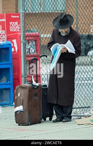 Ein orthodoxer Mann, der den Sabbat in Williamsburg verbrachte, wartet auf einen Bus und verbringt seine Zeit damit, ein religiöses Manuskript zu studieren. In Brooklyn, New York. Stockfoto