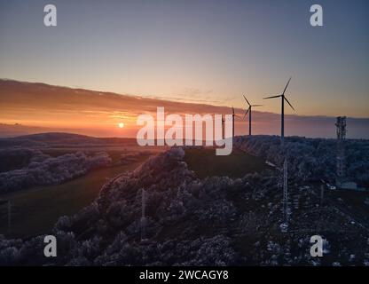 Luftlandschaftsfotografie von Sonnenaufgang über frostbedeckter Natur mit Windturbinen. Windmühle in sanftem Morgenlicht mit eisigen Bäumen. Konzept von Stockfoto