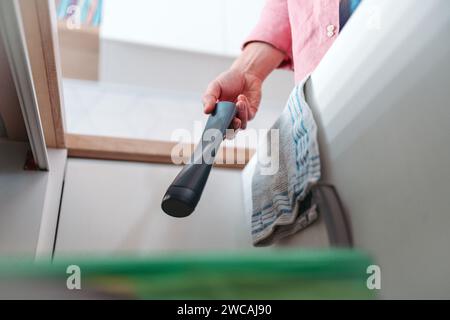 Mann wirft Plastikflasche in den Recyclingbehälter. Sortieren von Abfällen nach Material in farbigen Abfallbehältern in der Küche. Stockfoto