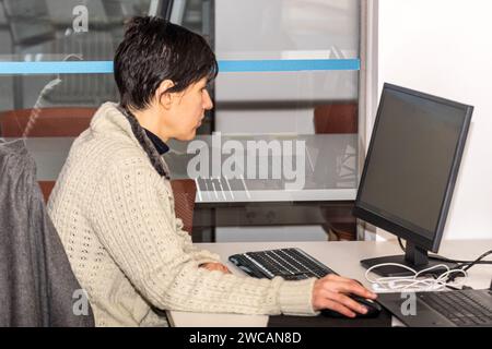 Konzentrierte kaukasische Frau, die im Büro vor dem Computer arbeitet. Seitenansicht Stockfoto