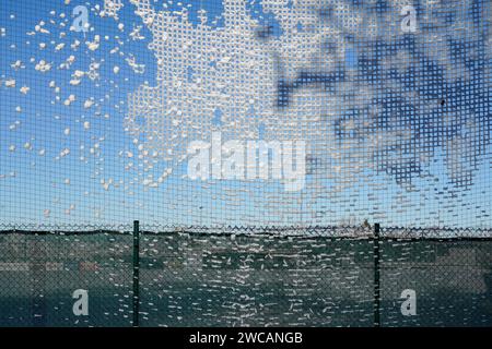 Winterspitze: Das schneegeschmückte Netz. Das Netz eines Fußballfeldes wird zur Leinwand für den Winter, während Schneeflocken ein zartes Muster an einem blauen Himmel weben. Stockfoto