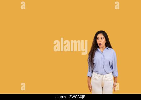 Überraschte junge Frau mit langen, welligen Haaren und breiten Augen, die ein blaues Hemd trägt Stockfoto