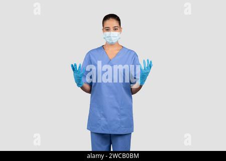 Eine zusammengesetzte Ärztin in blauen Peelings und Schutzhandschuhen hebt ihre Hände Stockfoto