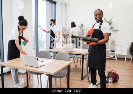 Afroamerikaner, der schwarze Schürze trägt und den Boden eines modernen Büros saugt. Stockfoto