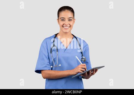 Eine freundliche junge Ärztin in blauen Peelings hält eine Tablette mit einem Stift Stockfoto