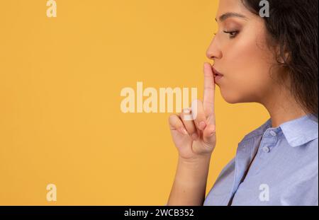 Seitenprofil einer jungen Frau mit lockigem Haar, die ihren Zeigefinger in einer 'shh'-Geste über die Lippen legt Stockfoto