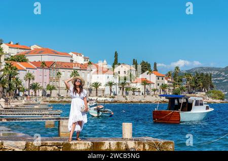 Vorderansicht einer wunderschönen jungen Frau mit Sommerkleid und Hut, die an der Küste in Korcula in Kroatien steht Stockfoto