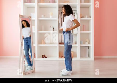 Eine junge Frau in Jeans, die im Spiegel sitzt, im rosafarbenen Zimmer Stockfoto