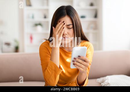 Eine beunruhigte junge asiatische Frau, die das Telefon in der Hand hält Stockfoto