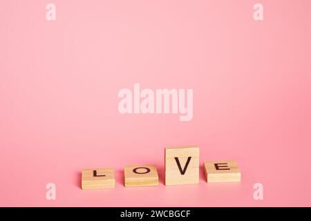 Liebe ist ein Wahlkonzept, Buchstabe V wie ein Häkchen. Das Wort Liebe besteht aus einzelnen Holzbuchstaben auf rosa Hintergrund mit Kopierraum. Valentinstag, 14. Februar. Stockfoto