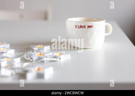 Weißer Becher mit der Aufschrift I love you, Erdbeeren auf einem weißen Frühstückstisch. Stockfoto