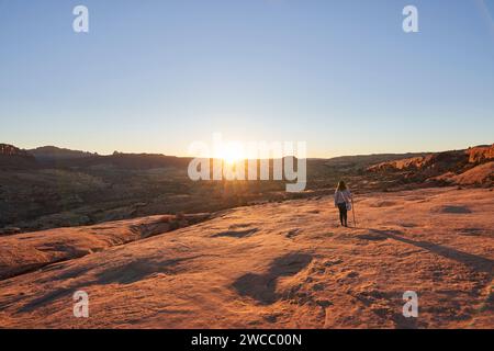 Die Sonne untergeht über den fernen Bergen, während eine Wanderer den goldenen Blick genießt. Stockfoto