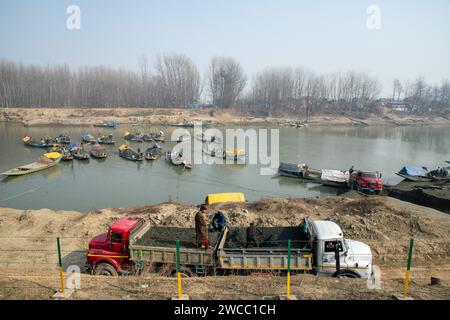 Srinagar, Indien, 15.01.2024, kaschmirische Männer extrahieren an einem kalten Wintertag in Srinagar Sand aus dem Fluss Jhelum. Eine beispiellose Trockenheit inmitten der intensiven Kälte hat dazu geführt, dass viele Gewässer in Kaschmir auf den Grund treffen, da das Wetterbüro bis zum 25. Januar im Allgemeinen trockenes Wetter vorhersagt. Wetterbeamte gaben an, dass die Region derzeit von einer außergewöhnlichen Dürre heimgesucht wird, mit einem Niederschlagsdefizit von 80 % ab Dezember 2023. Das anhaltende trockene Wetter hat jedoch bei den Menschen, die mit Landwirtschaft und Gartenbau in Verbindung stehen, ernste Besorgnis erregt, da Experten diese Wetterveränderungen in Verbindung bringen Stockfoto