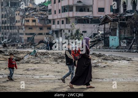 Gaza-Stadt, Palästinensische Gebiete. Januar 2024. Eine Palästinenserin geht mit Kindern durch das zerstörte Viertel Scheich Radwan in Gaza-Stadt, nach hundert Tagen des Isarel-Hamas-Krieges. Quelle: Omar Ishaq/dpa/Alamy Live News Stockfoto