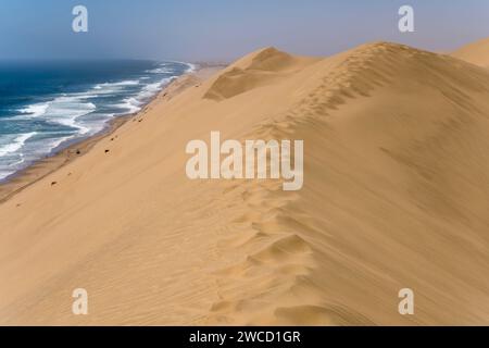 Küstenlandschaft mit Fußspuren am Dünenrand am Ufer der Wüste Naukluft, aufgenommen im hellen Licht des späten Frühlings in der Nähe von Sandwich Harbour, Namibia, Afrika Stockfoto