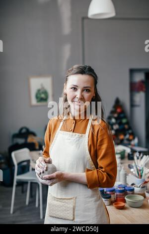 Porträt eines wunderschönen lächelnden Werkstattleiters für Keramik. Eine Töpferin mittleren Alters mit Ton in den Händen Stockfoto