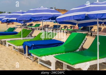 Bunte hölzerne Sonnenschirme und Liegestühle am Sandstrand des Meeres Stockfoto