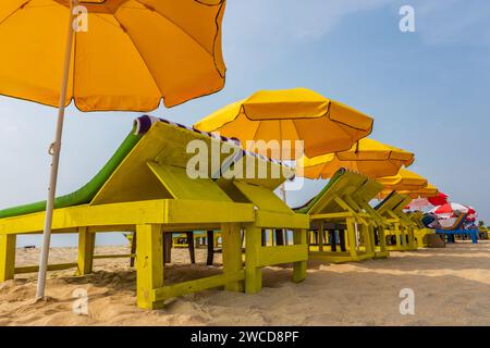 Bunte hölzerne Sonnenschirme und Liegestühle am Sandstrand des Meeres Stockfoto