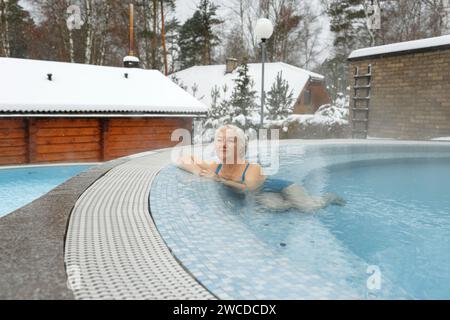 Eine ältere Frau nimmt im Winter Wasserbehandlungen in einem warmen Hydromassagebecken im Freien auf. Glückliche Frau, die sich im Pool erholt. Stockfoto