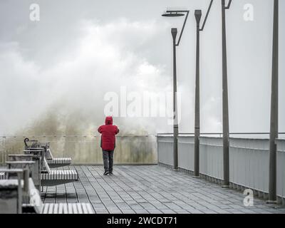 Ein Tourist, der ein Foto von einer großen stürzenden Welle macht, die die Pier-Front trifft Stockfoto