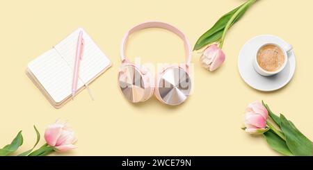 Moderne Kopfhörer, Notebook, Tasse Kaffee und Tulpenblüten auf hellgelbem Hintergrund Stockfoto