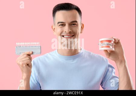 Schöner Mann, der Zähne hält Farbproben und Kiefermodell mit Zahnspangen auf rosa Hintergrund, Nahaufnahme Stockfoto