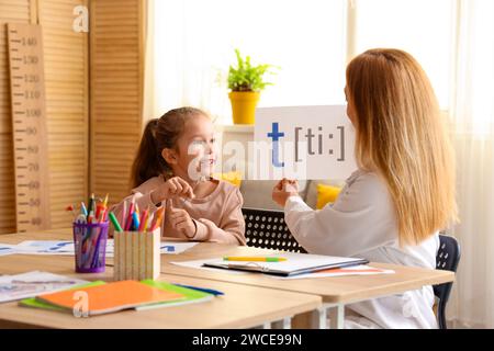 Niedliches kleines Mädchen mit Logopädin, die am Tisch im Büro einen Brief ausspricht Stockfoto