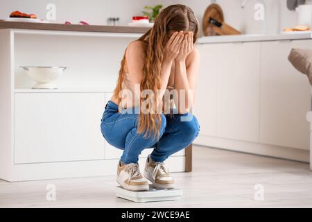 Verärgerte junge Frau in engen Jeans auf Waage zu Hause. Gewichtszunahme-Konzept Stockfoto