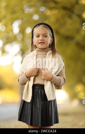 Kindertag. Fröhliches kleines Mädchen 5-6 Jahre alt posiert und lächelt draußen vor der Kamera und steht am Baum im Herbstpark. Stilvoller Zartpressdruck Stockfoto