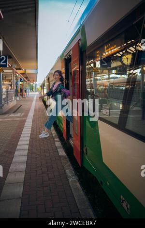 Kaukasisch aussehendes Mädchen, das in letzter Minute vor der Abfahrt in den Zug springt. Wunderschönes Mädchen posiert an einem sonnigen Sommertag vor der Tür des Zuges Stockfoto