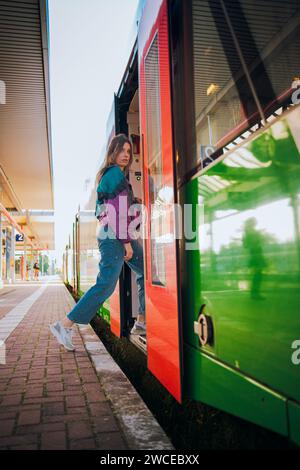 Kaukasisch aussehendes Mädchen, das in letzter Minute vor der Abfahrt in den Zug springt. Wunderschönes Mädchen posiert an einem sonnigen Sommertag vor der Tür des Zuges Stockfoto