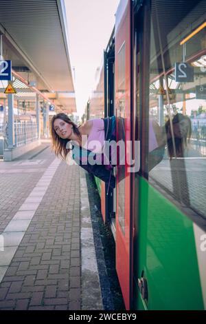 Kaukasisch aussehendes Mädchen, das in letzter Minute vor der Abfahrt in den Zug springt. Wunderschönes Mädchen posiert an einem sonnigen Sommertag vor der Tür des Zuges Stockfoto