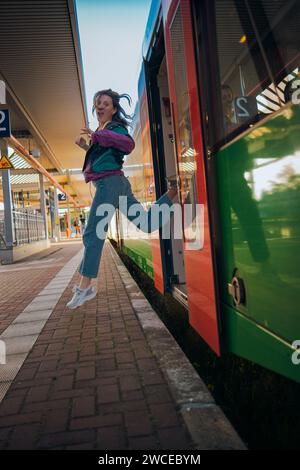 Kaukasisch aussehendes Mädchen, das in letzter Minute vor der Abfahrt in den Zug springt. Wunderschönes Mädchen posiert an einem sonnigen Sommertag vor der Tür des Zuges Stockfoto